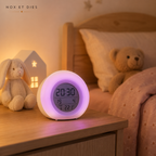 Réveil veilleuse Boule violette posée sur une table de chevet dans une chambre d'enfant avec peluches