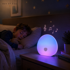 Veilleuse portable Bruma Nox et Dies posée sur une table de nuit, lumière bleu-violet diffusée pendant qu'un enfant dort, sons apaisants illustrés par des notes de musique