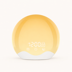 Packshot du réveil lumineux 2 waves sur fond blanc. Le produit présente une forme sphérique avec une base blanche ondulée (évoquant des vagues) et une face avant jaune orangée. L'écran digital LED affiche "AM 12:00.00" et trois icônes tactiles (alarme, soleil, lune) sont alignées en bas.