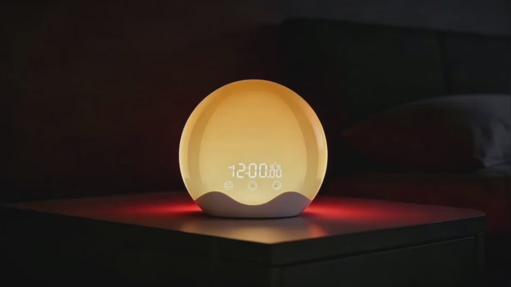 Animation du réveil simulateur d'aube 2 waves dans l'obscurité, émettant une lumière orange tamisée qui imite le lever du soleil. Sa base diffuse une lueur rouge subtile, et l'heure s'affiche en blanc lumineux. Parfait pour se réveiller en douceur sans lumière agressive.
